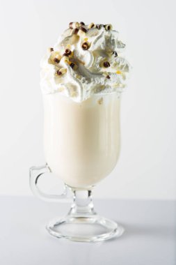Glass cup with handle containing white chocolate, whipped cream and chocolate chips.
