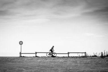 LE BARCARES, FRANCE - 11 Nisan 2022: Genç bir adam köy plajı yakınlarındaki yaya geçidi boyunca bisiklet sürüyor.