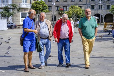 PONTEVEDRA, İspanya - 10 Ağustos 2022: Parlak renkli giyinmiş bir grup yaşlı adam şehrin yaya sokaklarından birinde geziniyor.