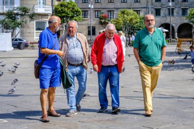 PONTEVEDRA, İspanya - 10 Ağustos 2022: Parlak renkli giyinmiş bir grup yaşlı adam şehrin yaya sokaklarından birinde geziniyor.
