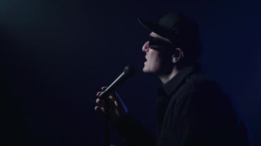 Karanlık bir arka planda şarkı söyleyen bir rap sanatçısının yakın çekimi. 4k yüksek çözünürlüklü görüntü. 