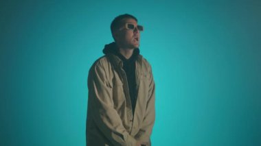 Mavi arka planda şarkı söyleyen bir rap sanatçısının orta boy fotoğrafı. 4k yüksek çözünürlüklü görüntü. 