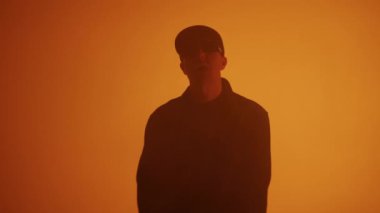 Turuncu arka planda şarkı söyleyen bir rap sanatçısının orta boy fotoğrafı. 4k yüksek çözünürlüklü görüntü. 