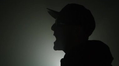 Karanlık bir arka planda şarkı söyleyen bir rap sanatçısının siluetini kapat. 4k yüksek çözünürlüklü görüntü.  