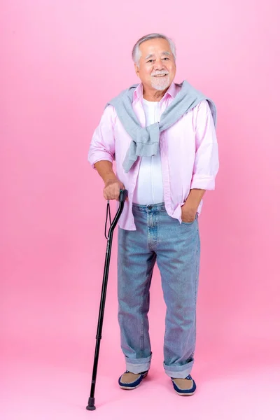 Retired asian elderly man happy walking with crutches pink background.