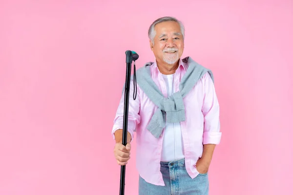 Traveling retired asian elderly man happy walking with crutches pink background.