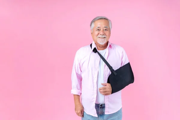 Retired elderly Asian man broken arm wear arm splint for treatment pink background.