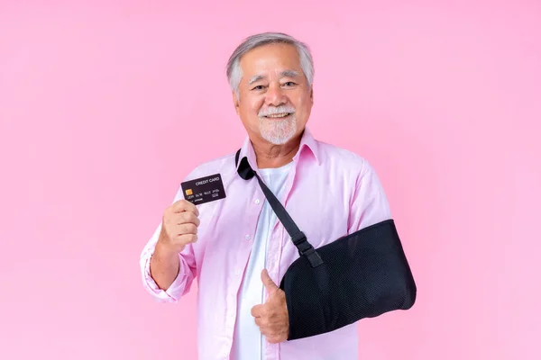 Traveling retired asian elderly man with hat broken arm wear arm splint for treatment and smiling and holding credit card for confident lifestyle, Old elderly male payment credit card medical care.