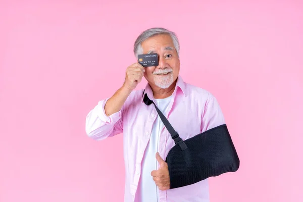Traveling retired asian elderly man with hat broken arm wear arm splint for treatment and smiling and holding credit card for confident lifestyle, Old elderly male payment credit card medical care.