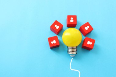 Eğitim ve insan kaynakları konsepti imajı. Yaratıcı fikir ve yenilik. Mavi arkaplan üzerinde ampul metaforu, tahta küpler ve insan simgeleri