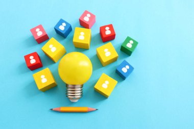 Eğitim ve insan kaynakları konsepti imajı. Yaratıcı fikir ve yenilik. Mavi arkaplan üzerinde ampul metaforu, tahta küpler ve insan simgeleri