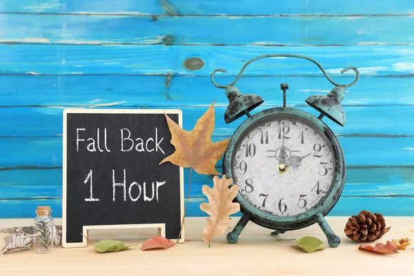 秋時間変更のイメージ コンセプトにフォールバックします 乾燥した葉と素朴な木製のテーブルにビンテージの目覚まし時計 — ストック写真