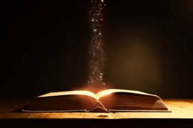 Tahta masanın üzerinde parıltılı kaplamalı açık antik kitabın sihirli görüntüsü.