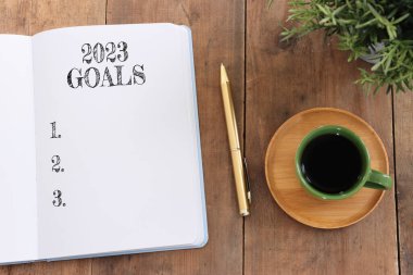 Üst görünüm iş konsepti 2023 gol listesi, defter, ahşap masa üzerinde bir fincan kahve.