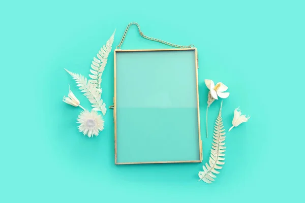 Top view image of white dry flowers and empty gold photo frame with copy space over pastel blue background .Flat lay