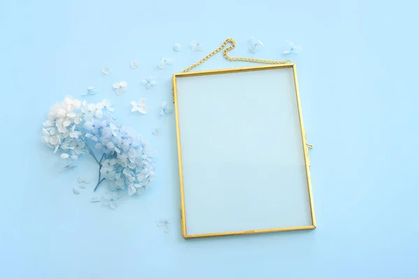 Top view image of blue dry flowers and empty gold photo frame with copy space over pastel background .Flat lay