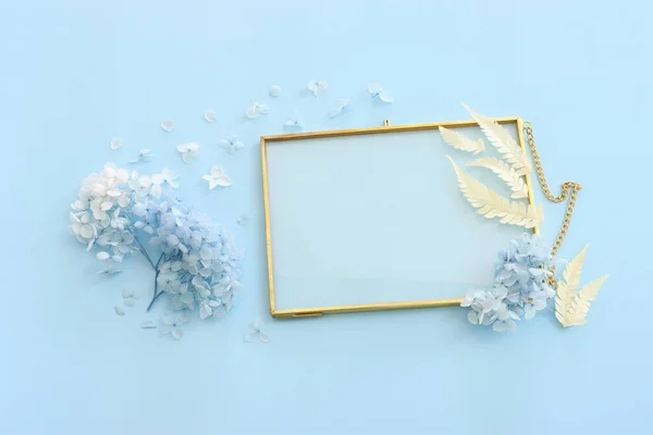 Top view image of blue dry flowers and empty gold photo frame with copy space over pastel background .Flat lay