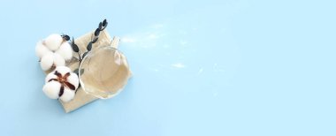 Top view of elegant perfume bottle with clean white cotton flower over pastel blue background. Cosmetics, fragrance and perfumery concept