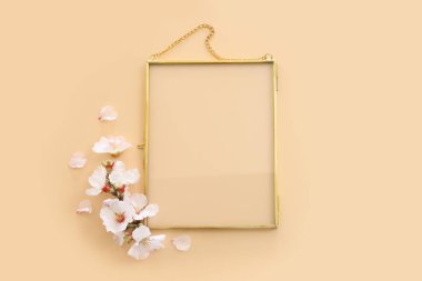 Badem çiçeği çiçeklerinin üst manzarası ve sarı pastel arkaplan üzerinde altın renkli boş çerçeve. Model oluşturmak için, alanı kopyala