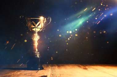 düşük anahtar görüntü Trophy üzerinde ahşap masa ve soyut glitter ışıkları ile koyu arka plan