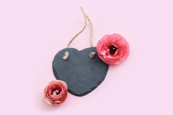 top view of pink flowers and heart shape slate stone board over pastel background. For mock up, copy space