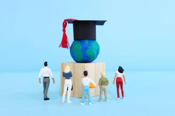 People looking at model of earth with graduation hat