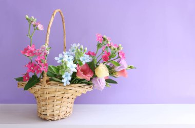 Hasır sepetteki narin pembe çiçeklerin resmi ahşap masa ve mor arka plan üzerinde
