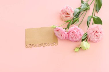 Top view image of pink flowers composition and empty note over pastel background
