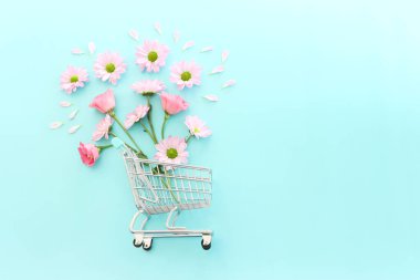 Pastel mavi arka planda çiçekler olan alışveriş arabası. Tatil alışverişi ve satış konsepti