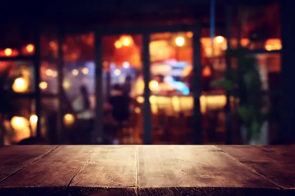 Bild Eines Holztisches Vor Abstrakt Verschwommenem Hintergrund Von Restaurantlichtern lizenzfreie Stockfotos