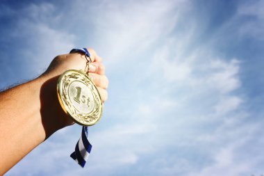 Adam el kaldırıyor, altın madalyayı gökyüzüne karşı tutuyor. ödül ve zafer konsepti