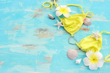 Kadın mayo bikini ve monoi çiçeğinin ahşap pastel mavi arka planda üst görüntüsü. Yaz tatili konsepti