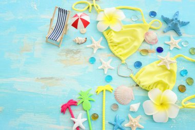 Kadın bikini, denizyıldızı, tekne ve monoi çiçeğinin ahşap pastel mavi arka planda üst görüntüsü. Yaz tatili konsepti