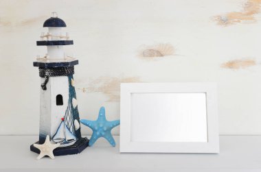 Deniz feneri, deniz yıldızı ve beyaz rafın üzerinde boş fotoğraf çerçevesi ve pastel ahşap arka plan. Model için.