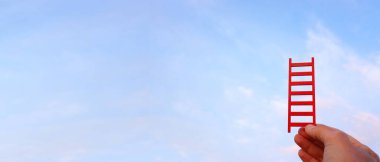 El ele tutuşan kırmızı merdiven gökyüzünün önünde. Yüksek hedefler ve başarı kavramı