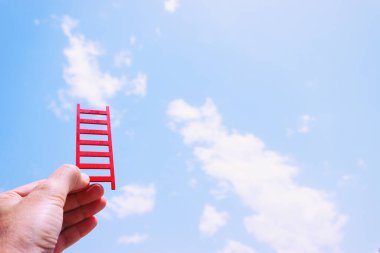 El ele tutuşan kırmızı merdiven gökyüzünün önünde. Yüksek hedefler ve başarı kavramı
