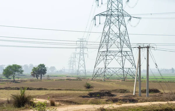 stock image Power lines over an agricultural field against clear sky horizon. High-voltage tower installed in a row on a field.