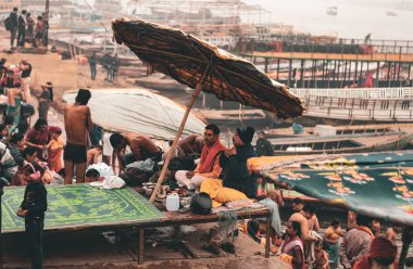 Kutsal bir keşiş, Varanasi ghat sehpasında oturan bir sadhu, sabahın erken saatlerinde bir şemsiyenin altında. Uzaktan çekilen fotoğraflar. Uttar Pradesh Hindistan 1 Ocak 2024