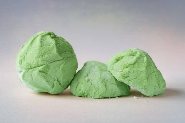 Green marshmallow. A whole and two halves of a green marshmallow on a colorful abstract background. Sweet dessert. Colored sweetness