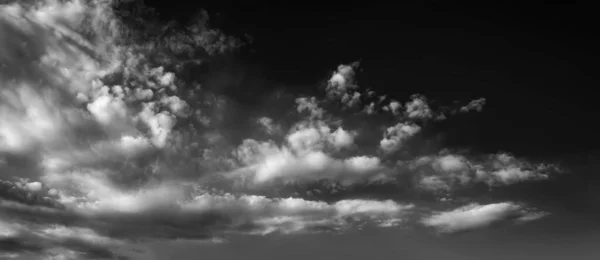 Panorama of white clouds on a dark dramatic sky. Storm wind clouds. Black and white sky template to create atmosphere