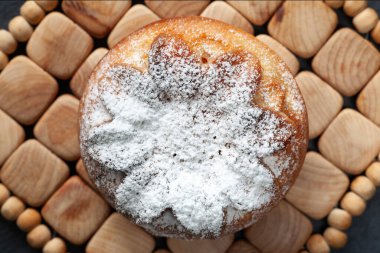 Taze kek. Çörek üzerine pudra şekeri serpilmiş. Tahta desenli yüzeydeki bir kekin üst görüntüsü. Ev yapımı pişirme.