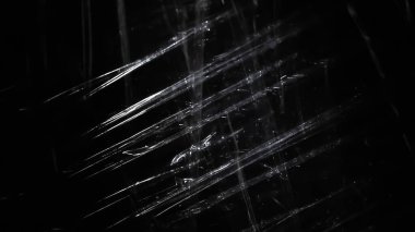 Soyut arkaplan. Islak, buruşmuş polietilen parıltısı. Siyaha sentetik sim. Seçici odak