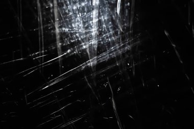 Abstract background. The shine of crumpled polyethylene. Synthetic shine on black. Selective focus