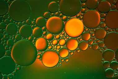 Yağ kabarcıkları. Sudaki yağ baloncuklarına yakın çekim. Yeşil-turuncu tonlarda soyut doku. Makro fotoğrafçılık