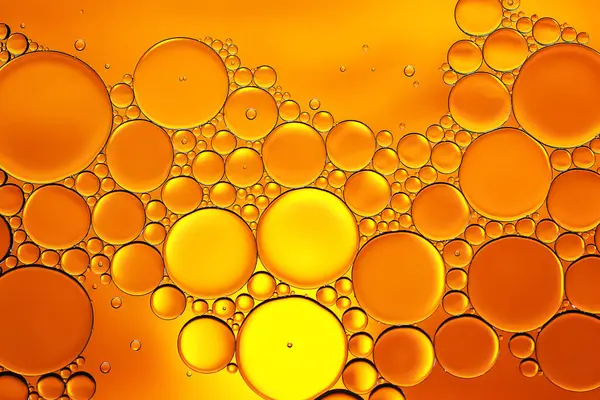 Yağ kabarcıkları. Su üzerindeki yağ kabarcıklarının altın tonlarında yakın plan çekimi. Soyut doku. Makro fotoğrafçılık