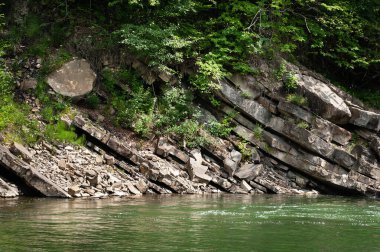 Dağ nehri. Uçurum nehrin üzerinde asılı. Kaya kıyısı. Dağlarda büyük taşlar