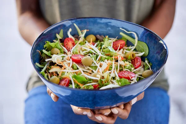 Hands of african american woman holding bowl with fresh salad of cabbage, tomato and green leaves. High angle view of healthy woman holding bowl of delicious and fresh salad. Vegan, dieting food concept.