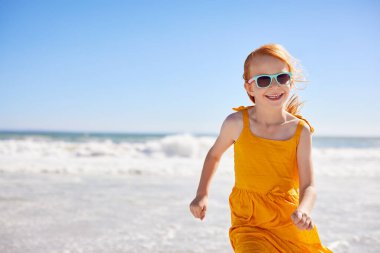 Sahilde fotokopi odasıyla koşan kızıl saçlı tatlı bir kadın. Deniz kıyısında güzel sarı bir elbiseyle yürürken güneş gözlüğü takan çilli mutlu küçük bir kızın portresi. Tropikal bölgelerde yaz tatili boyunca eğlenen kadın çocuk