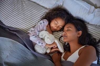 Çok ırklı barışçıl bir anne ve küçük tatlı bir kız yatakta sarılıp yatıyor. Huzurlu bir anne ve küçük tatlı bir kızın dinlenme anı, birbirlerine sıkıca sarıldıkları. Hindistan 'ı seven anne ve küçük kızının yumuşak yastıkta uyumasının en iyi görüntüsü.