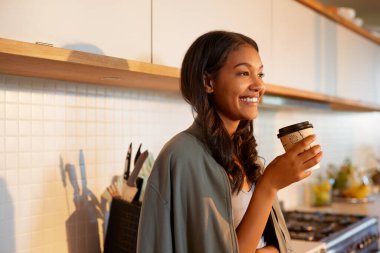 İspanyol genç kadın sabah kahvesini mutfakta içerken gülümsüyor. Karışık ırk kadını sabah kahvesini tek kullanımlık bardakta içerken ayakta ve mutfak platformunda yaslanırken içiyor. Çok ırklı bir kız huzur içinde bir kahve molası veriyor.